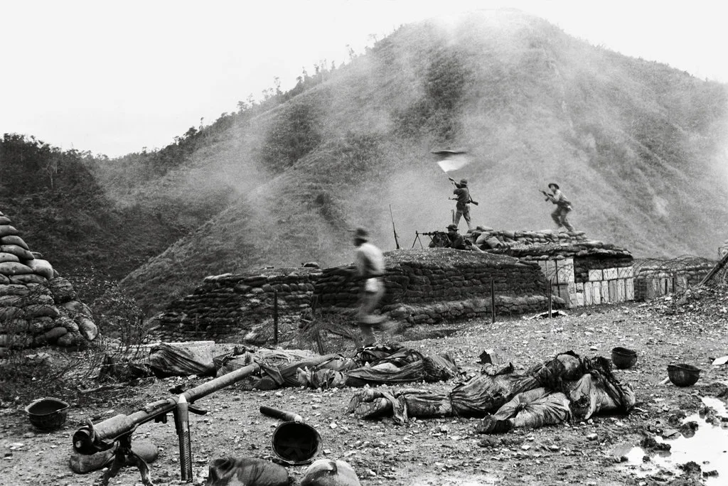 Vietnam War Battle, Combat Scene, Black and White Photography, Soldiers in Action, Urgent Movement, Fortified Bunker, Sandbag Defense, Mountainous Terrain, Warzone Chaos, Soldier Urgency, Firing Weapon, Defensive Position, Smoke and Dust, War Realities, Discarded Equipment, Intense Battle Conditions, Frontline Fragility, Combat Environment, War Violence, Historical Military Conflict